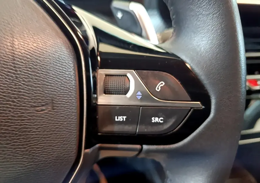 Gros plan sur les commandes gauche du volant cuir du Peugeot 208 2023, boutons de téléphone et sélection audio visibles.