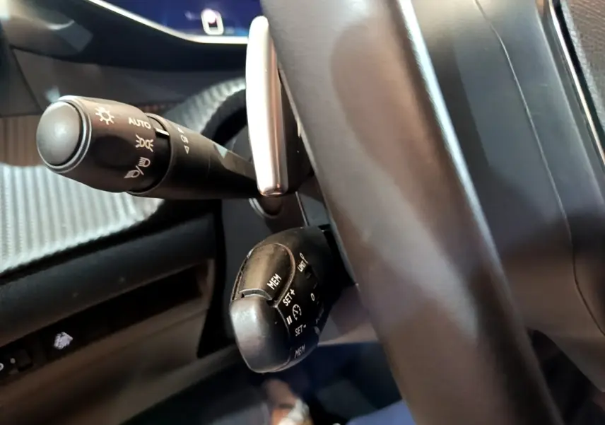 Gros plan sur la commande de régulateur de vitesse et le commodo d'éclairage à gauche du volant noir dans une Peugeot 208 jaune.