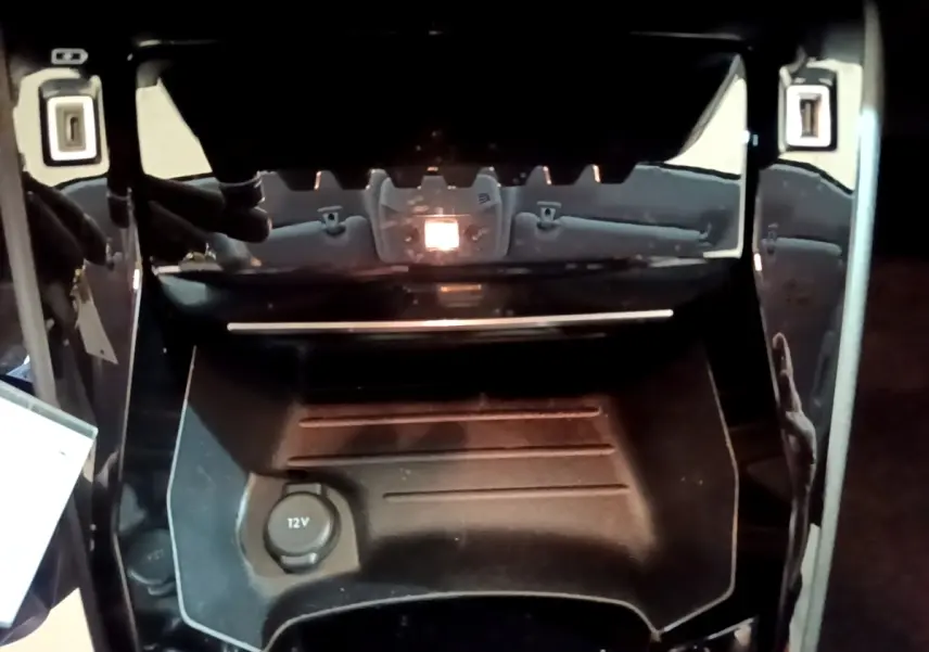 Gros plan sur la console centrale noire de la Peugeot 208, avec prise 12V visible au centre.