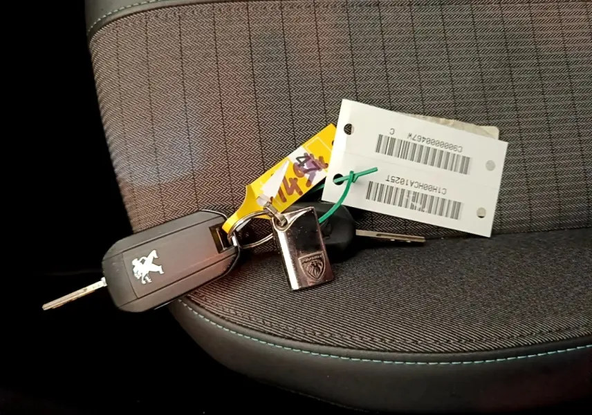 Gros plan sur une clé Peugeot posée sur un siège tissu gris avec surpiqûres bleues à l'intérieur d'une 208 jaune.