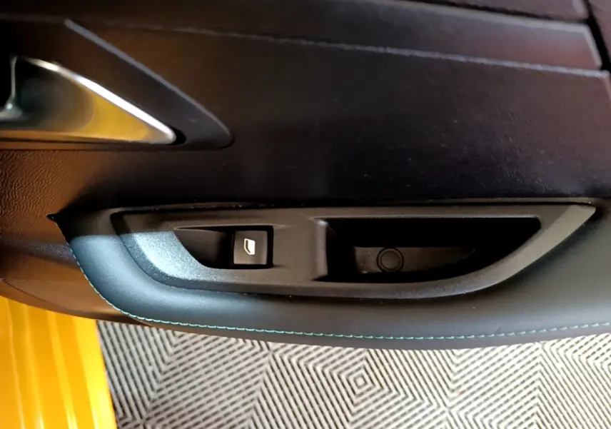 Détail de la commande de lève-vitre sur la porte intérieure d'une Peugeot 208 jaune, finition Allure Pack.