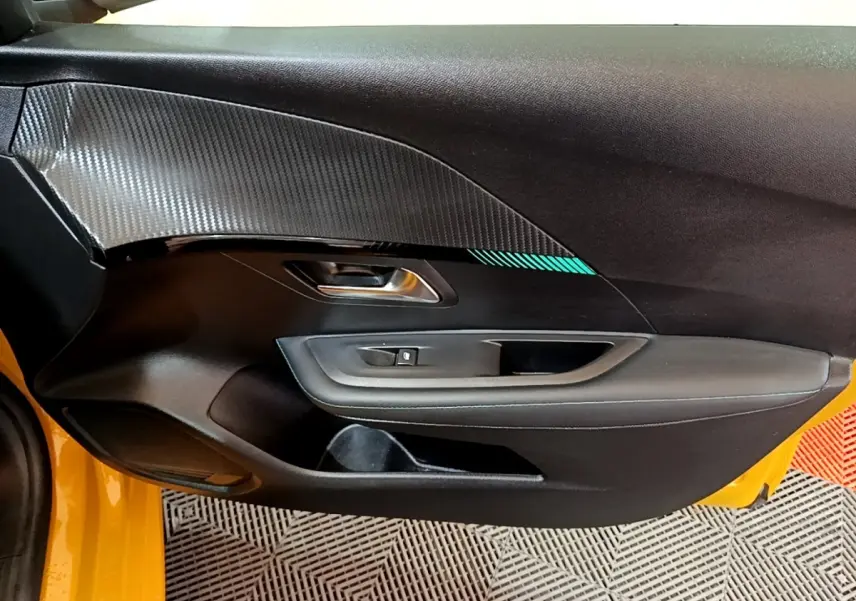 Vue intérieure côté gauche de la porte avant d'une Peugeot 208 jaune avec insert décoratif gris et poignée métallique.