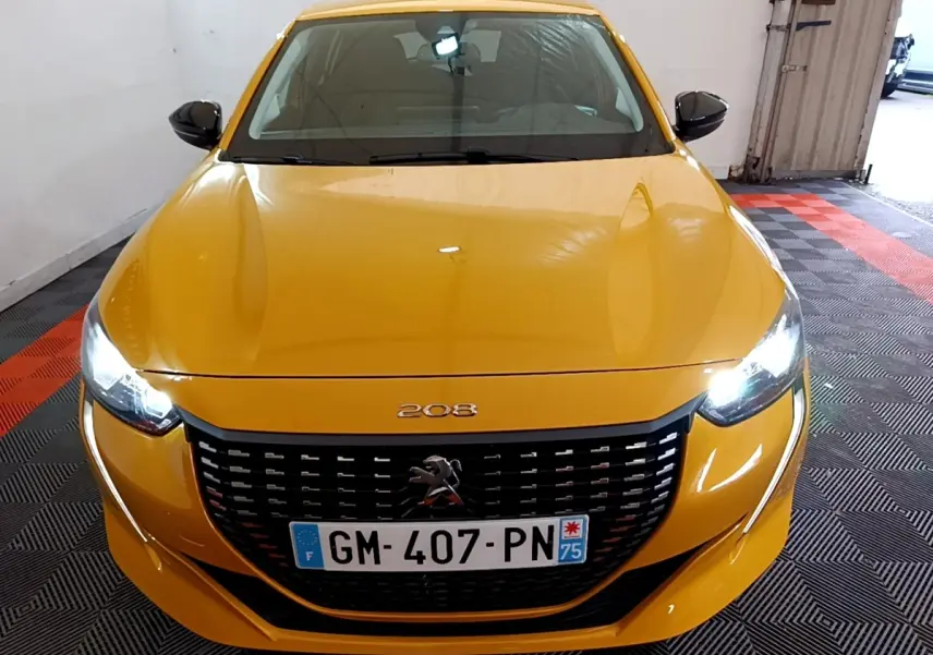 Vue avant d'une Peugeot 208 jaune 2023 avec phares LED allumés et calandre noire distinctive.