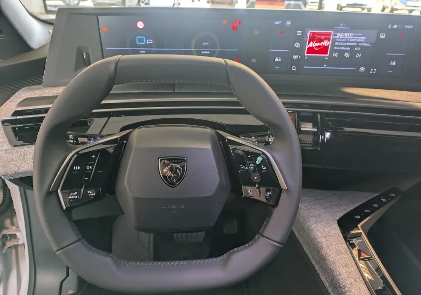Volant cuir noir et tableau de bord numérique double écran HD du Peugeot 5008 blanc Okenite 2025, vue intérieure avant centrée.