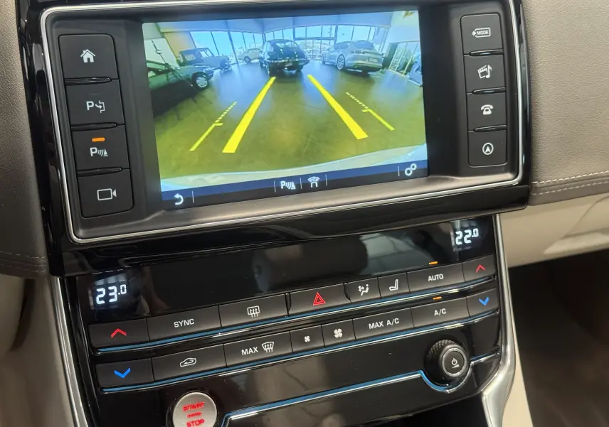 Vue rapprochée de l'écran central et de la console d'une Jaguar XE beige, affichant la caméra de recul et la climatisation digitale.