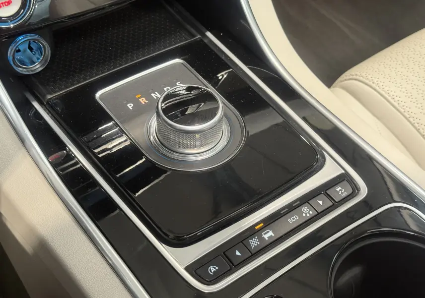 Vue rapprochée de la console centrale noire avec sélecteur rotatif de boîte auto sur Jaguar XE beige 2015.