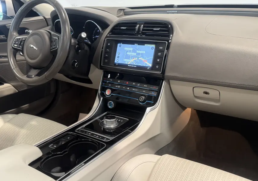 Intérieur beige clair de la Jaguar XE 20d Prestige 2015, vue côté conducteur sur tableau de bord et console centrale avec écran tactile.