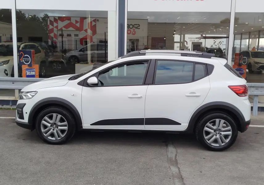 Profil côté gauche d'une Dacia Sandero Stepway blanche glacier avec barres de toit noires et protections latérales noires.
