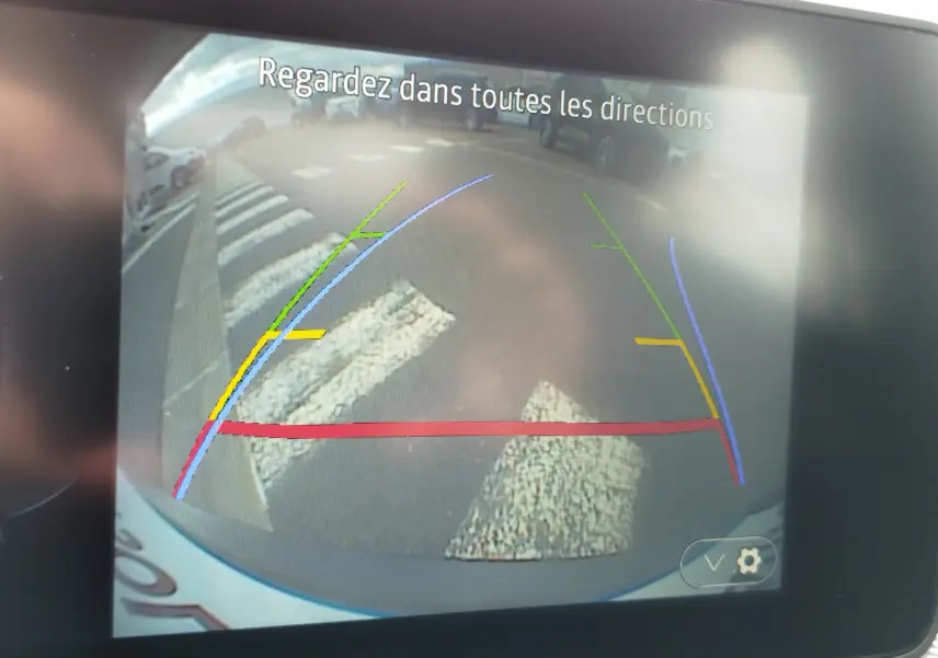 Affichage de la caméra de recul d'une Dacia Sandero Stepway blanche, avec lignes de guidage colorées et marquage au sol visible.