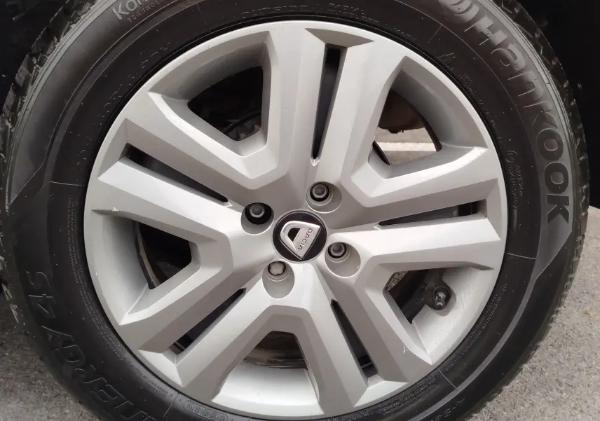 Gros plan sur la jante argentée de la roue d'une Dacia Sandero Stepway blanche, avec logo central visible.