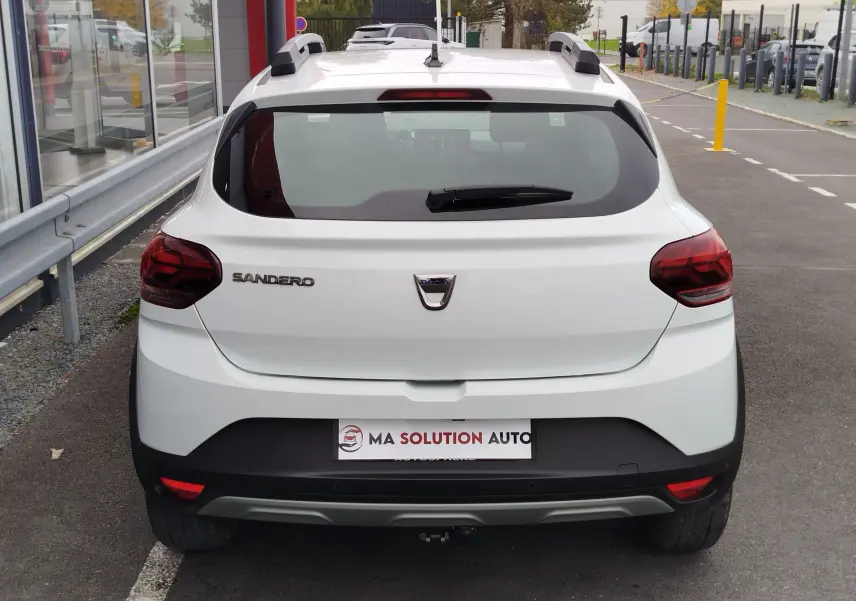 Vue arrière d'une Dacia Sandero Stepway blanche Glacier avec barres de toit et feux arrière foncés.