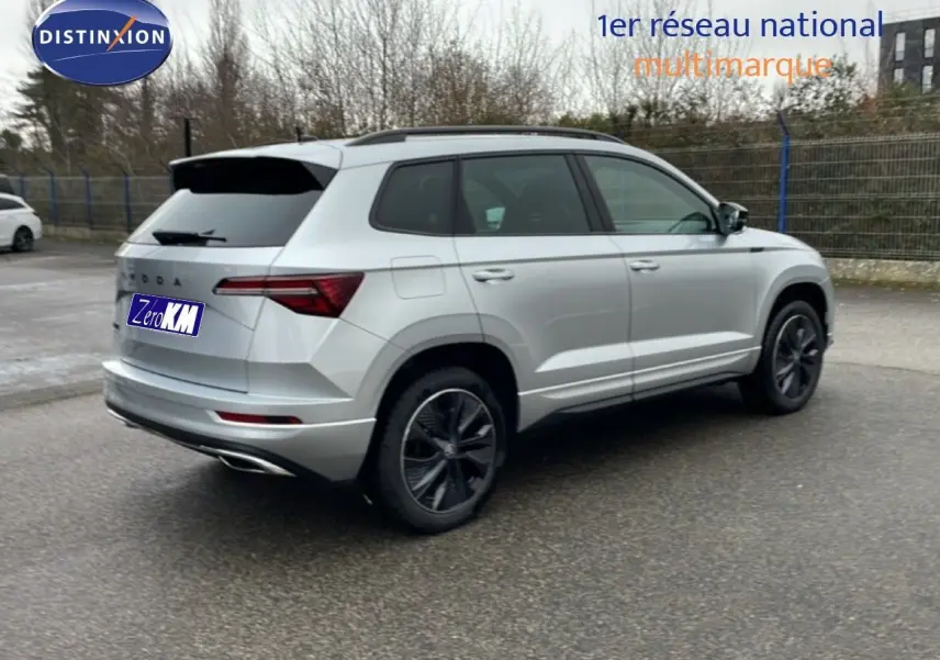 Vue 3/4 arrière droite d’un Skoda Karoq gris argent métallisé avec jantes noires et toit ouvrant, stationné en extérieur.