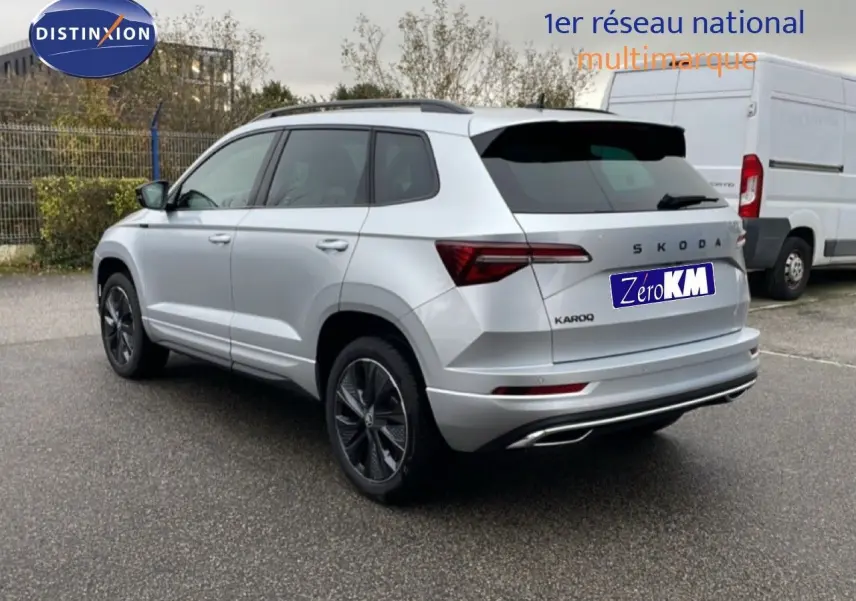 Vue 3/4 arrière droite d’un Skoda Karoq gris argent métallisé 2025 avec jantes noires et détails sportifs.