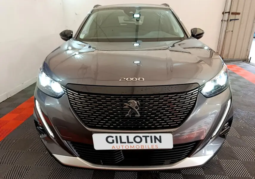 Vue frontale d'un Peugeot 2008 gris foncé avec calandre noire et phares LED allumés en intérieur showroom.
