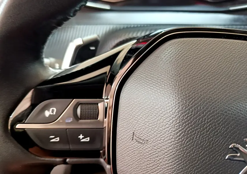 Gros plan sur le volant cuir multifonctions noir du Peugeot 2008 gris foncé, avec commandes intégrées visibles.