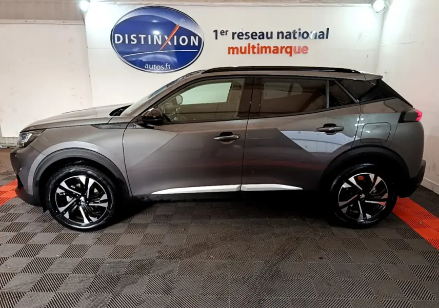 Profil droit d'un Peugeot 2008 gris foncé 2022 avec jantes noires et toit noir, en intérieur sur sol damier.