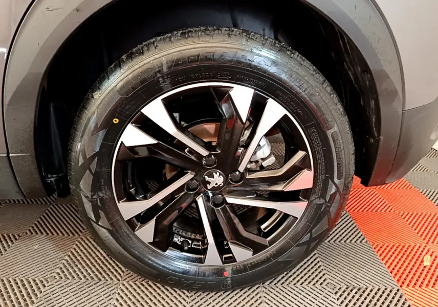 Gros plan sur la roue avant droite du Peugeot 2008 gris foncé, mettant en valeur la jante noire et argentée au design moderne.