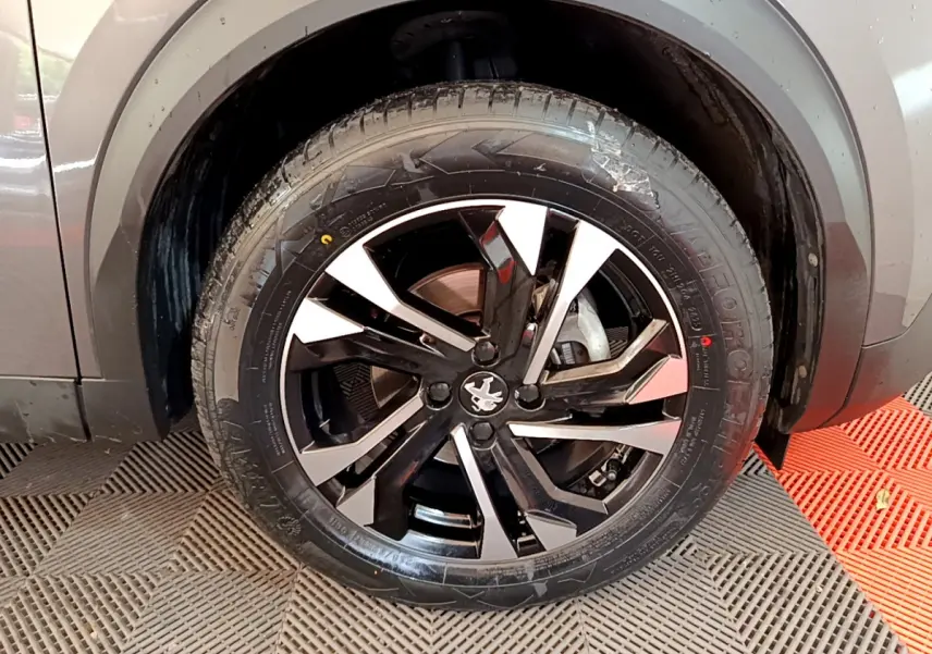Gros plan sur la roue avant droite d’un Peugeot 2008 gris foncé, avec jante alliage noire et argentée au design moderne.