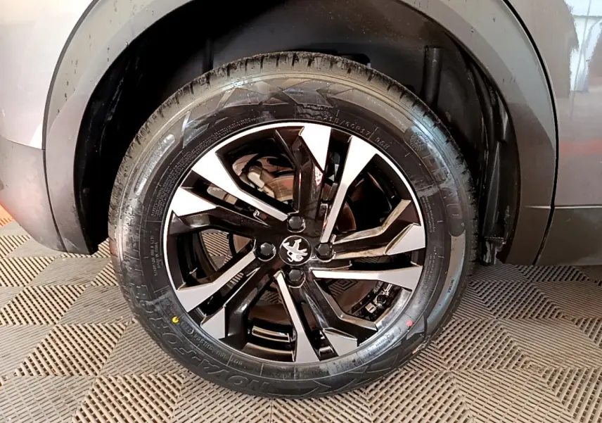 Gros plan sur la roue avant gauche d’un Peugeot 2008 gris foncé, avec jante alliage noire et argentée au design moderne.