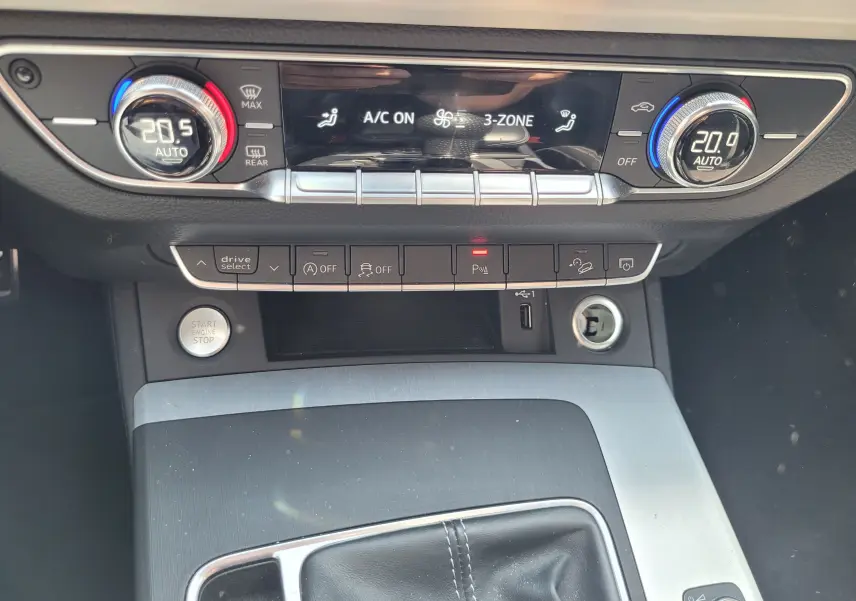 Vue rapprochée de la console centrale de l'Audi Q5 noire 2018, affichant la climatisation automatique 3 zones et les commandes de conduite.