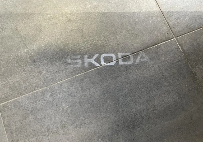 Projection lumineuse du logo SKODA au sol sur un carrelage gris, sans véhicule visible.