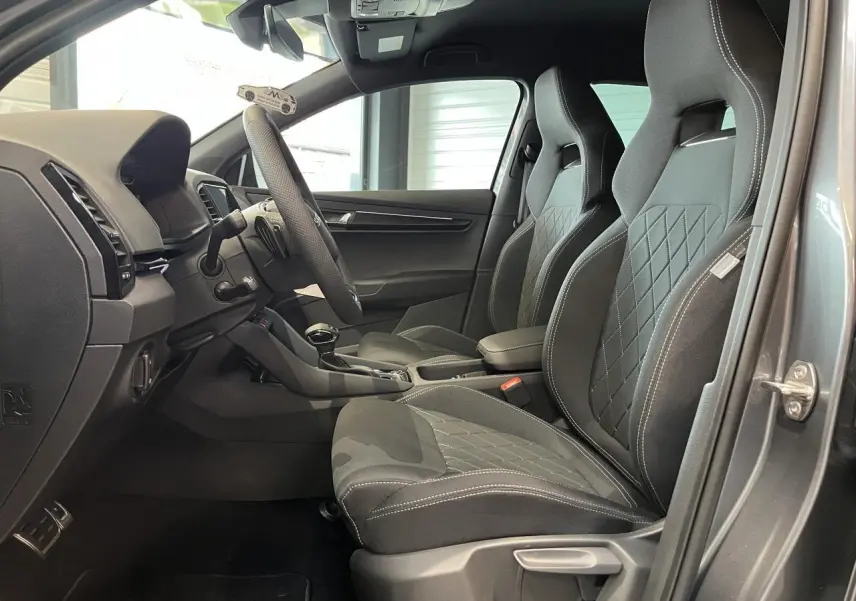 Vue intérieure côté gauche du Skoda Karoq gris 2025, mettant en valeur les sièges sport noirs avec surpiqûres blanches.