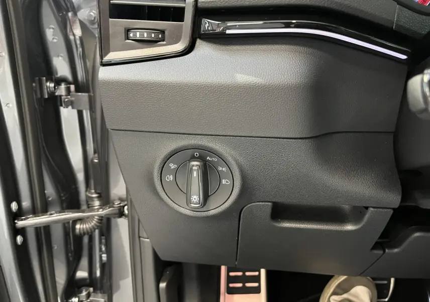 Gros plan sur le bouton de commande des phares côté gauche du tableau de bord d'un Skoda Karoq gris 2025 Sportline.