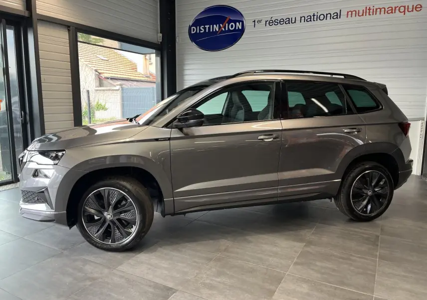 SUV SKODA KAROQ gris en profil droit dans un showroom avec jantes alliage noires et toit ouvrant noir.