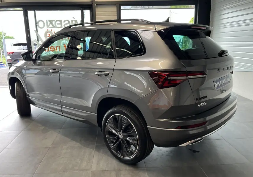 Vue 3/4 arrière droite du SUV SKODA KAROQ gris métallisé avec jantes alliage 19'' Sagitarius anthracite et toit noir.