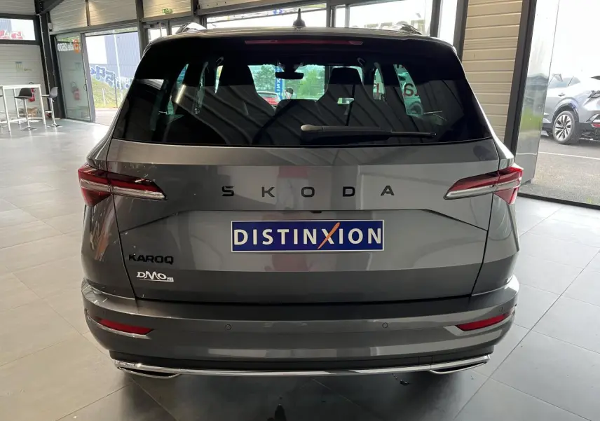 Vue arrière d'un SUV SKODA KAROQ gris métallisé exposé en showroom avec logo Distinxion sur le hayon.