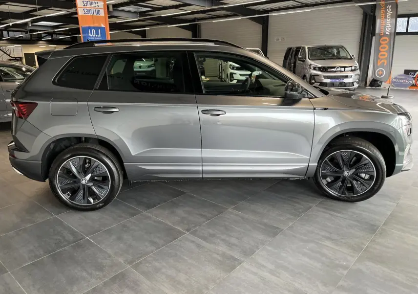 Profil côté gauche d'un SUV SKODA KAROQ Sportline gris perle avec jantes alliage noires et toit noir en intérieur showroom.