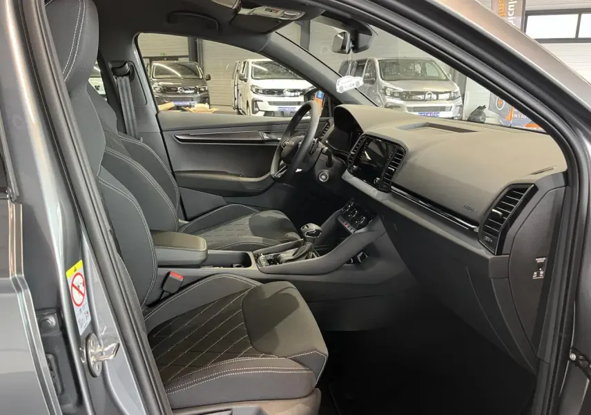 Intérieur avant droit du Skoda Karoq gris 2025, sièges sport noirs avec surpiqûres blanches et tableau de bord moderne.