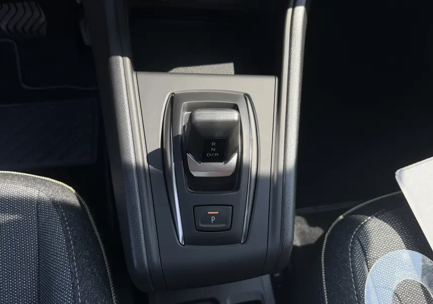 Vue de dessus du levier de vitesses automatique noir sur console centrale grise, entouré de sièges tissu gris avec surpiqûres jaunes.