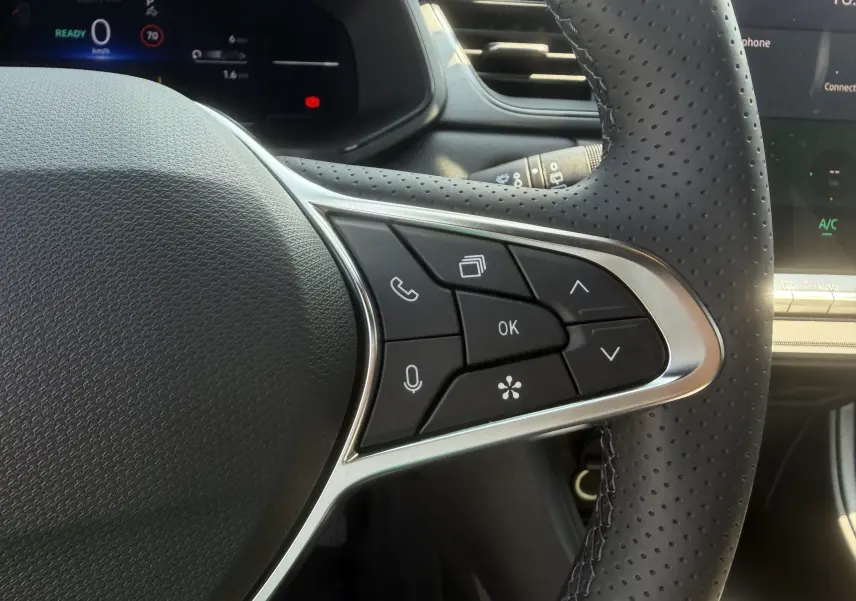 Gros plan sur les commandes multifonctions à droite du volant perforé noir du Renault Captur gris Cassiopée, tableau de bord numérique en arrière-plan.
