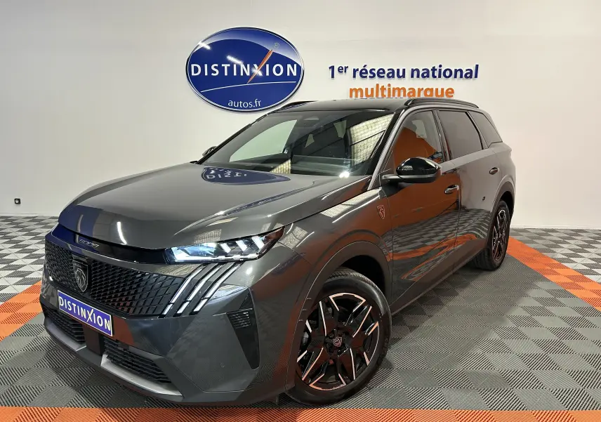 Peugeot 5008 gris titane en 3/4 avant droit, avec jantes noires et phares LED allumés, en showroom.