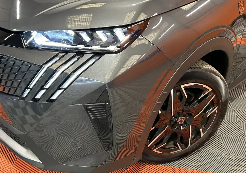 Gros plan sur l’avant droit du Peugeot 5008 gris titane, mettant en valeur le phare LED et la jante noire à inserts métallisés.