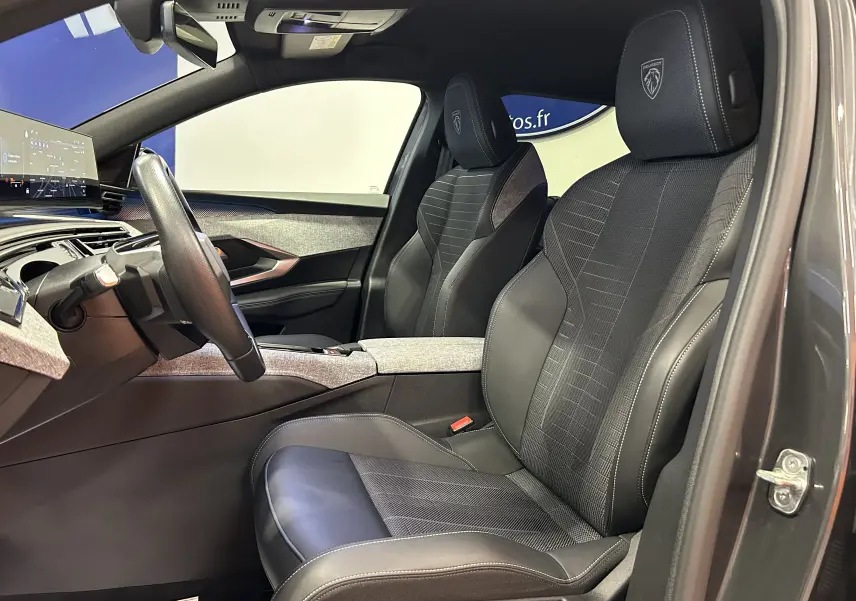 Vue intérieure côté conducteur du Peugeot 5008 III Hybrid 145 e-DCS6 GT, sièges noirs avec logo Peugeot brodé sur les appuie-têtes.