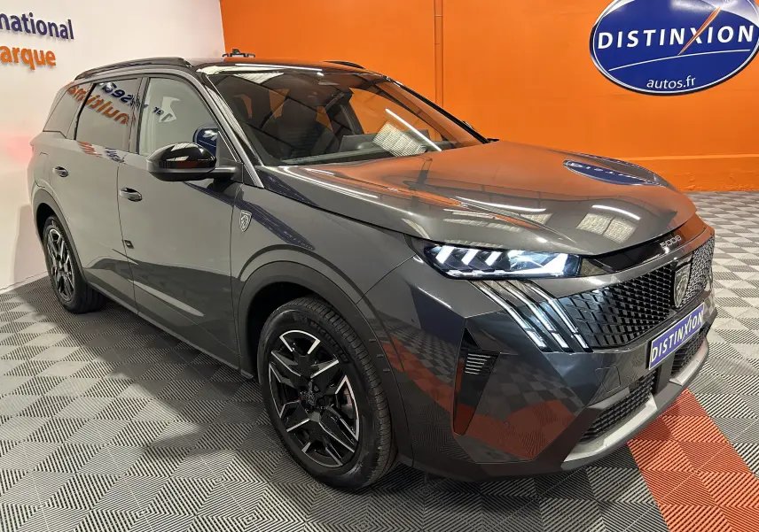 Peugeot 5008 III Hybrid gris titane en 3/4 avant droit, avec phares LED allumés et jantes noires biton.