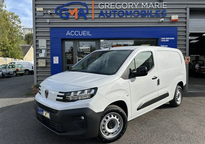 Fourgon blanc Peugeot Partner BlueHDi 2025 vu en 3/4 avant droit devant un garage GMA.