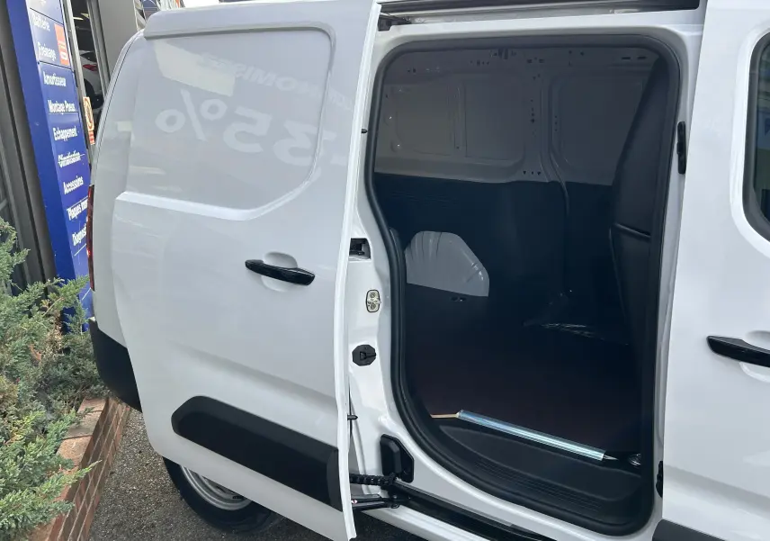 Vue latérale gauche du Peugeot Partner Fourgon blanc 2025 avec porte coulissante ouverte révélant plancher bois intérieur.
