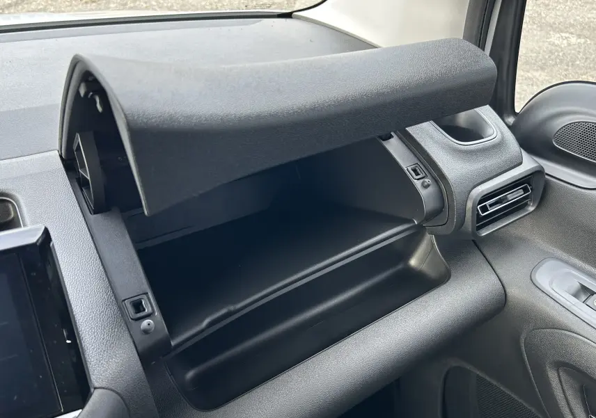 Gros plan sur la boîte à gants ouverte côté passager du Peugeot Partner Fourgon blanc, montrant l'intérieur noir du tableau de bord.