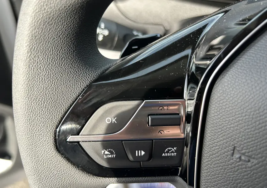 Gros plan sur les commandes du volant noir du Peugeot Partner Fourgon blanc, avec boutons de limitation et assistance.