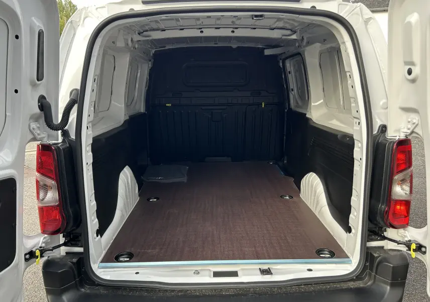 Vue arrière du Peugeot Partner Fourgon blanc 2025 avec portes ouvertes et plancher bois visible dans l'espace de chargement.
