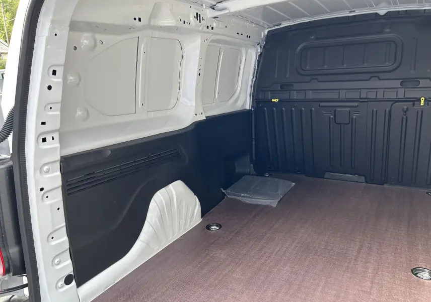 Intérieur du fourgon Peugeot Partner blanc vu de l'arrière, plancher bois et parois noires visibles.