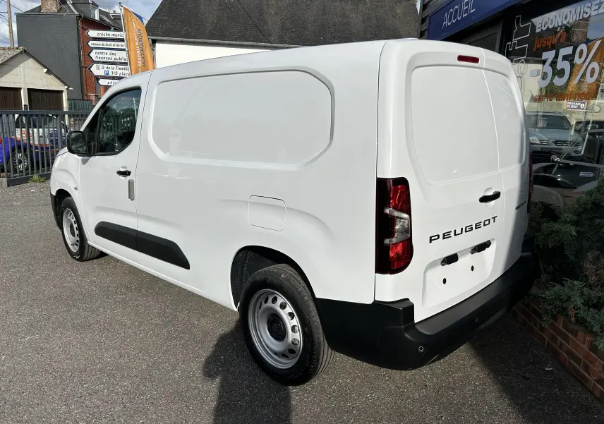 Vue 3/4 arrière droite d’un Peugeot Partner Fourgon blanc avec protections noires et logo arrière visible.