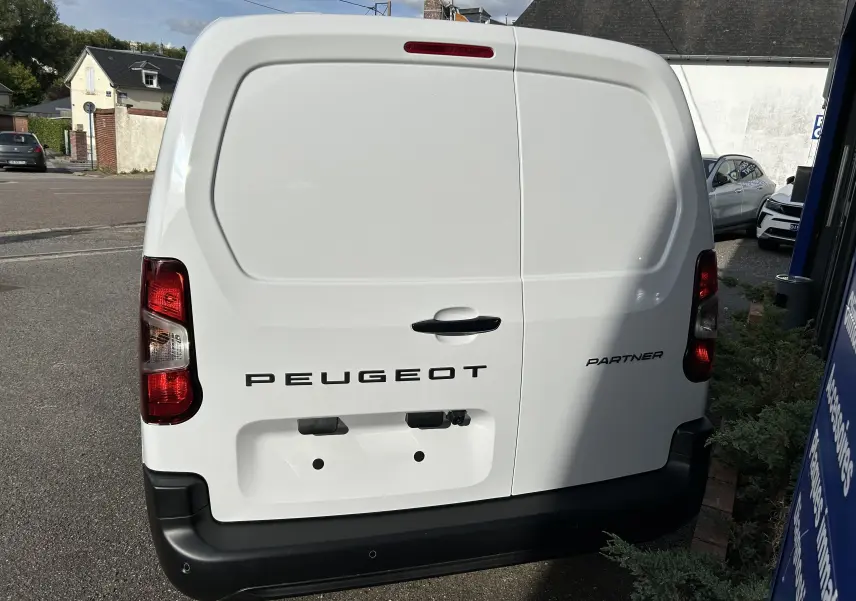 Vue arrière d'un Peugeot Partner Fourgon blanc avec logo noir et feux arrière rouges sur parking extérieur.