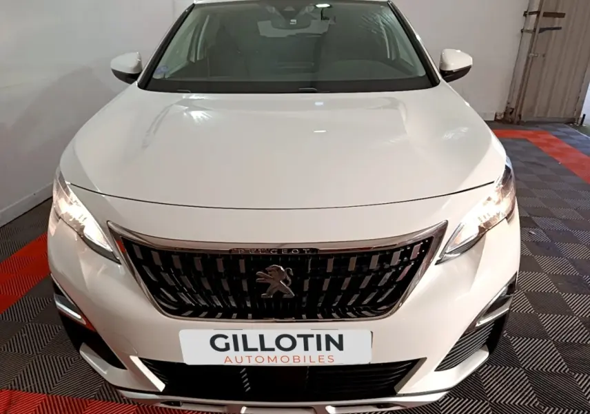 Vue avant d'un Peugeot 3008 blanc hybride rechargeable avec calandre noire et phares allumés dans un garage.