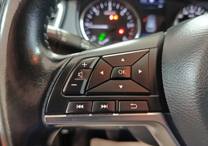 Gros plan sur les commandes multifonctions noires du volant cuir du Nissan Qashqai 2019, tableau de bord flou en arrière-plan.