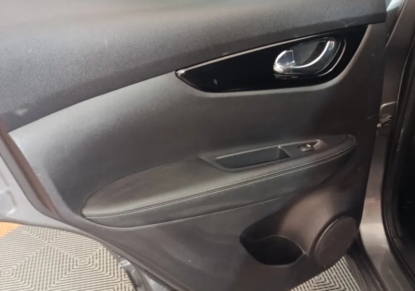 Vue rapprochée de la porte intérieure côté conducteur du Nissan Qashqai gris clair, avec poignée chrome et commande de vitre.