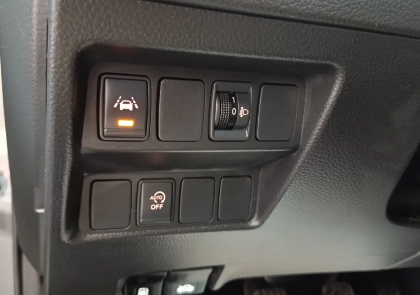 Gros plan sur les commandes de réglage des phares et d'aide à la conduite du tableau de bord du Nissan Qashqai gris clair 2019.